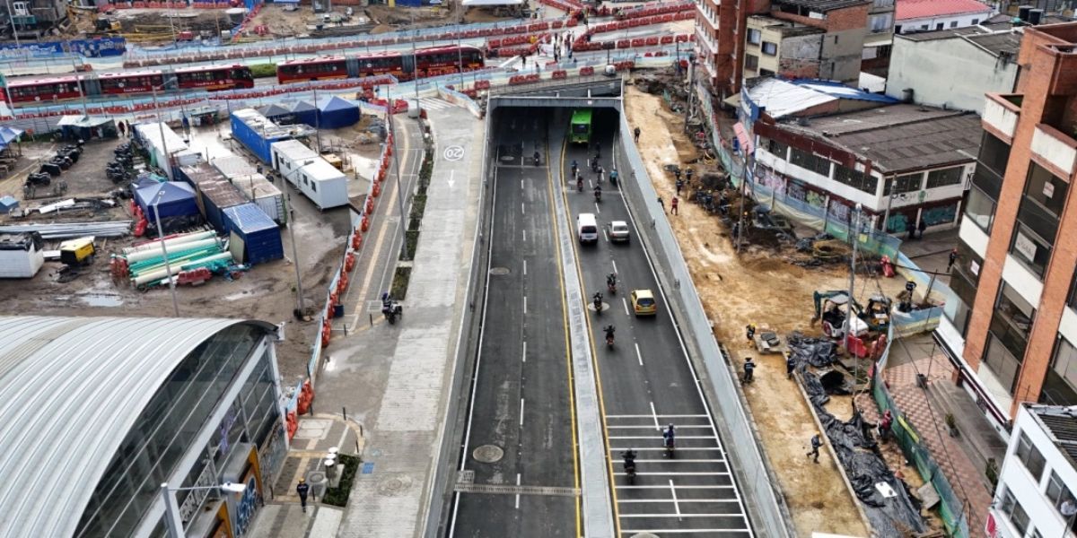 Vista aérea de un paso deprimido con vehículos en circulación, obras de construcción, buses, edificios y maquinaria a los lados.